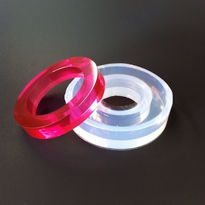 May include: Two silicone molds for making resin rings. One mold is clear and the other is pink.