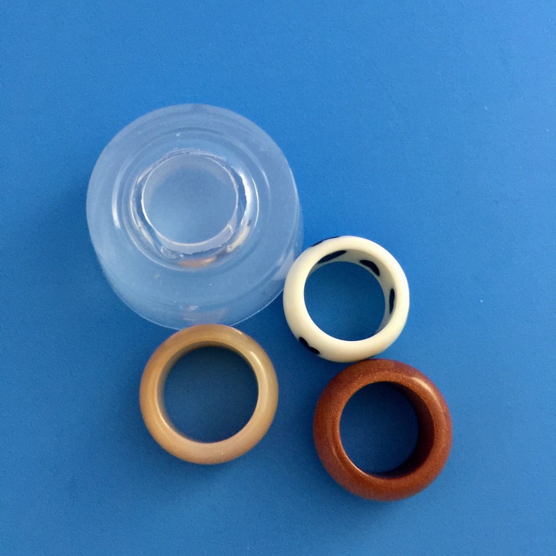 May include: Three resin rings, one with a white and black polka dot pattern, one brown, and one beige. A clear silicone mold for making rings is also shown.