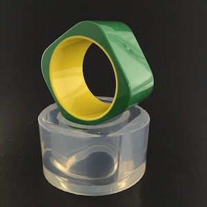 May include: A green and yellow bangle bracelet in a clear silicone mold. The bangle is square shaped with rounded edges.
