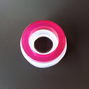 May include: A pink and white plastic ring with a hole in the center. The ring is made of two layers, with the top layer being pink and the bottom layer being white.