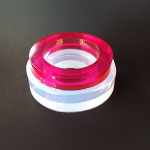 May include: A set of two silicone molds for making resin rings. The top mold is pink and the bottom mold is clear.