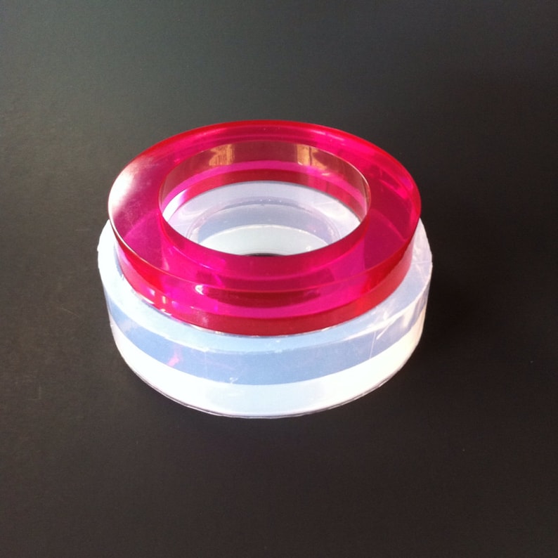 May include: A set of two silicone molds for making resin rings. The top mold is pink and the bottom mold is clear.
