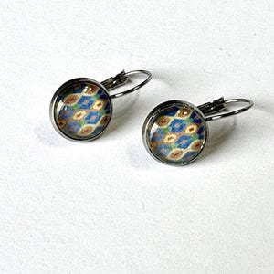 May include: A pair of round, silver-toned leverback earrings. Each earring features a domed glass cabochon with a colorful pattern of blue, gold, and brown shapes. The earrings are set against a white background.