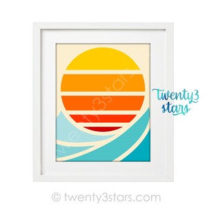 Puede incluir: Una impresi&oacute;n enmarcada con una puesta de sol de estilo retro sobre las olas. El sol es un c&iacute;rculo con rayas naranjas, amarillas y rojas. Las olas son azules y blancas.
