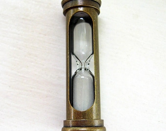 May include: A vintage hourglass in a bronze-toned metal casing. The glass vessel contains white sand, seen through the open sides. The design of the hourglass is reminiscent of antique timekeeping devices.