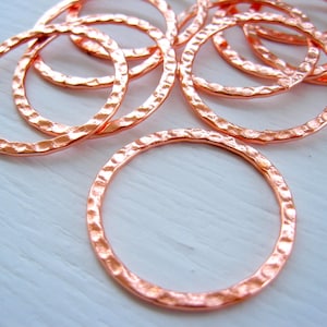 May include: Close-up of several hammered copper rings. The rings have a textured surface and a warm, reddish-brown color. The rings are circular and appear to be handmade, perfect for jewelry making or other craft projects.