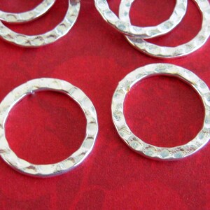 Peut inclure: Gros plan sur plusieurs anneaux en m&eacute;tal argent&eacute; martel&eacute;, sur fond rouge. Les anneaux ont une surface textur&eacute;e et une forme circulaire. La texture martel&eacute;e leur donne un aspect rustique et artisanal. Ces anneaux pourraient &ecirc;tre utilis&eacute;s pour la fabrication de bijoux ou d'autres projets d'artisanat.