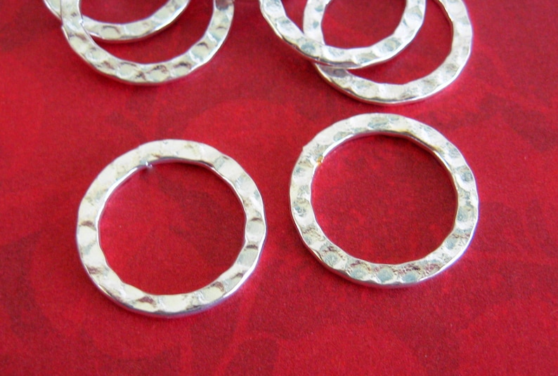 Peut inclure: Gros plan sur plusieurs anneaux en m&eacute;tal argent&eacute; martel&eacute;, sur fond rouge. Les anneaux ont une surface textur&eacute;e et une forme circulaire. La texture martel&eacute;e leur donne un aspect rustique et artisanal. Ces anneaux pourraient &ecirc;tre utilis&eacute;s pour la fabrication de bijoux ou d'autres projets d'artisanat.