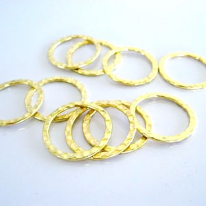 May include: A collection of eight circular gold-colored metal rings featuring a hammered, textured surface. Each ring has a consistent thin band design with a reflective finish, arranged in a loose cluster on a plain, light-colored surface.
