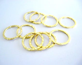 Peut inclure: Un ensemble de huit anneaux métalliques circulaires de couleur dorée présentant une surface martelée et texturée. Chaque anneau possède un design fin et uniforme avec une finition réfléchissante, disposé en groupe sur une surface claire.