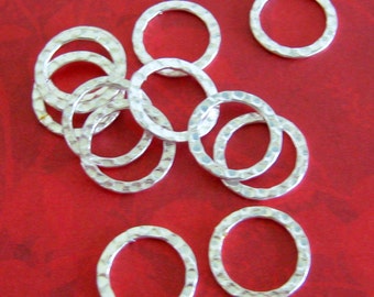 May include: A collection of silver-colored hammered metal rings, scattered on a red surface. The rings have a textured, dimpled surface and a circular shape. The image is well-lit, highlighting the metallic sheen of the rings.