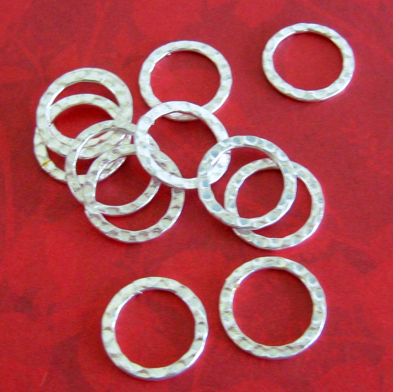 Peut inclure: Plusieurs anneaux en m&eacute;tal argent&eacute; martel&eacute;, dispos&eacute;s sur une surface rouge. Les anneaux pr&eacute;sentent une surface textur&eacute;e et alv&eacute;ol&eacute;e, de forme circulaire. L'image est bien &eacute;clair&eacute;e, mettant en valeur l'&eacute;clat m&eacute;tallique des anneaux.