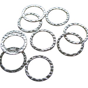 May include: A collection of eight circular metal rings with a silver-toned finish. Each ring features a distinct hammered texture along its surface, creating a series of small, reflective indentations that catch the light across the metal.