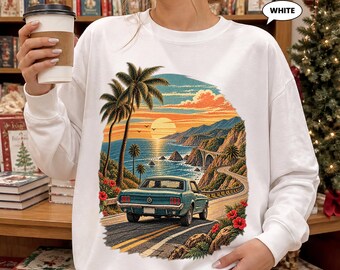 Könnte beinhalten: Ein weißes Langarm-Sweatshirt mit einem Grafikdruck eines türkisfarbenen Oldtimers auf einer Küstenstraße bei Sonnenuntergang. Das Motiv zeigt Palmen, felsige Klippen, eine Brücke und rote Hibiskusblüten. Das Sweatshirt hat einen Rundhalsausschnitt.