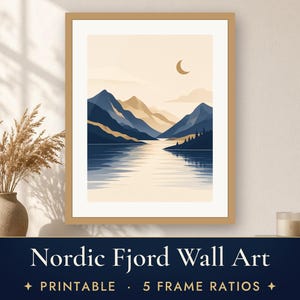 May include: A framed wall art print featuring a landscape illustration of mountains and a lake with a crescent moon in a beige sky. The artwork displays deep blue and tan tones with a reflection on the water surface and a light wood frame.