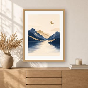 May include: A framed wall art print featuring a landscape illustration of dark blue mountains and a calm lake under a pale sky with a crescent moon. The artwork is displayed in a light wood frame, showcasing a serene scene with layered peaks.