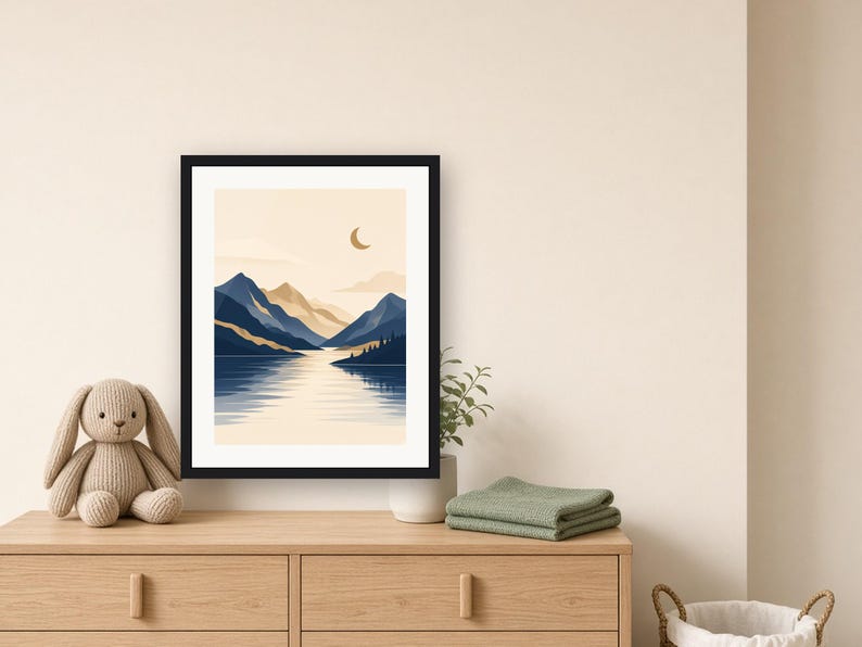 May include: A framed wall art print featuring a landscape illustration of dark blue mountains, a calm lake, and a crescent moon against a light beige sky. The artwork is enclosed in a simple black frame, showcasing a serene nature scene with layered peaks and reflections on the water surface.