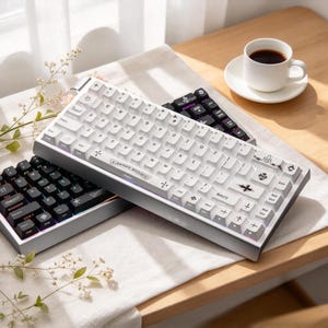 May include: A mechanical keyboard with white keycaps featuring black gothic-style symbols and text, including a prominent cross design on the shift key. A second black keyboard with backlit keys is partially visible underneath the white one.