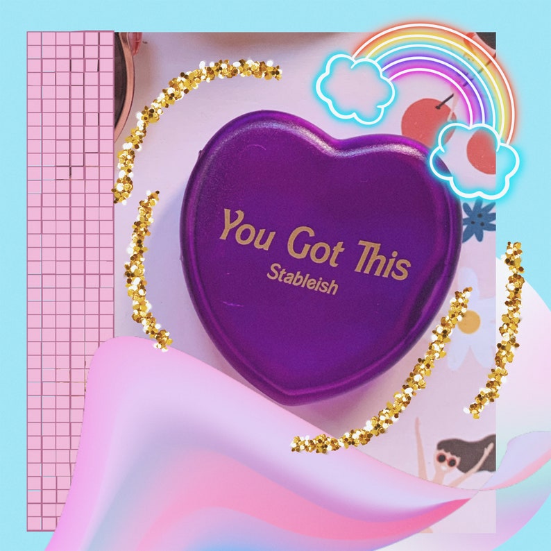 May include: Purple heart-shaped compact with gold glitter around the edges. The compact has the text "You Got This Stableish" in gold lettering.