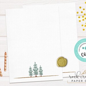May include: A blank white card with a gold border and a line of small green trees at the bottom. The card is on a white wood background with gold glitter and two gold candles.