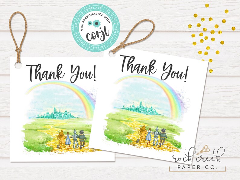 May include: Two printable thank you tags featuring a watercolor illustration of the yellow brick road from the Wizard of Oz. The illustration includes the characters Dorothy, the Scarecrow, the Tin Man, and the Cowardly Lion walking down the road towards the Emerald City. A rainbow arches over the city. The text "Thank You!" is printed on each tag.