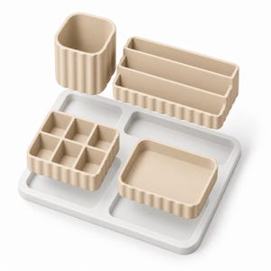 May include: A beige desk organizer set featuring a tall cylindrical cup, a tiered rectangular tray, a six-compartment square tray, and a single-compartment rectangular tray, all arranged on a white rectangular base with recessed sections.