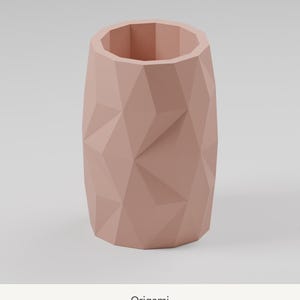 May include: A dusty rose cylindrical vase featuring a faceted, geometric exterior surface with sharp, angular planes. The vessel has an open top and a hollow interior, displaying a consistent matte finish throughout its entire structure.