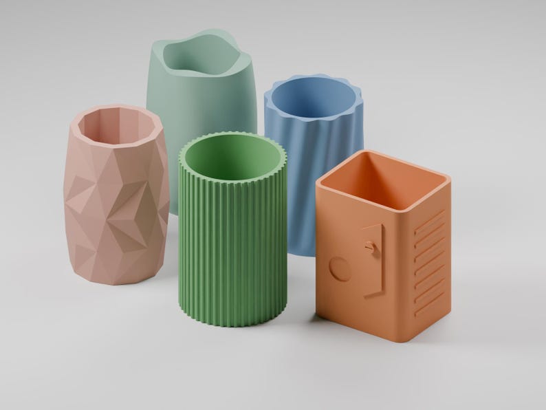 May include: A collection of five cylindrical desk organizers in various pastel colors. The set includes a pink geometric faceted holder, a light green organic shape, a green ribbed container, a blue fluted vessel, and an orange locker-style box.