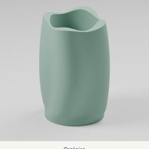 May include: A sage green vase with a smooth, matte finish and an irregular, undulating rim. The vessel features a cylindrical body with soft, flowing curves and a wide opening at the top. The word Org&aacute;nico is printed below the object.
