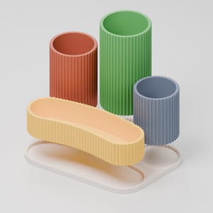Puede incluir: Un conjunto organizador de escritorio con tres recipientes cil&iacute;ndricos acanalados en terracota, verde y azul, junto a una bandeja ovalada alargada acanalada en amarillo claro, sobre una base blanca con un borde acanalado a juego.
