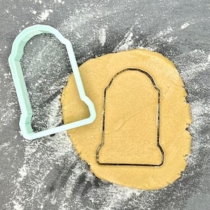 Może przedstawiać: Niebieska plastikowa foremka do ciasteczek w kształcie nagrobka, z brązowym ciastem do ciasteczek, które jest wycinane foremką.