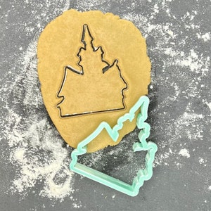 Może przedstawiać: Zielona plastikowa foremka do ciasteczek w kształcie zamku, na brązowym kółku ciasta.