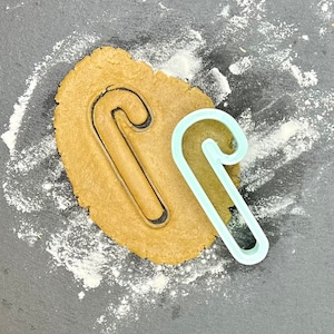 Puede incluir: Un cortador de galletas de caramelo de color azul claro sobre una superficie negra con un círculo de masa de galleta marrón y harina blanca espolvoreada alrededor.