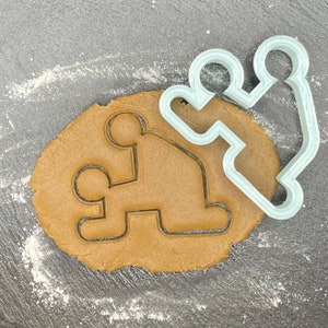May include: A silver cookie cutter in the shape of two people holding hands, with a brown cookie dough cutout in the same shape.