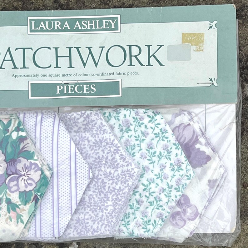 Pode incluir: Um pacote de pe&ccedil;as de tecido patchwork Laura Ashley. O pacote cont&eacute;m v&aacute;rias pe&ccedil;as de tecido com desenhos florais e estampados em tons de roxo, verde e branco. O pacote diz "PATCHWORK" e "PIECES".