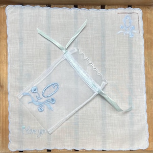 Op de afbeelding: Een witte zakdoek met een geschulpte rand en lichtblauwe rand. Het heeft geborduurde bloemmotieven en de letter "O" in lichtblauw. De woorden "I love you" zijn geborduurd. Een bijpassend zakje is inbegrepen.