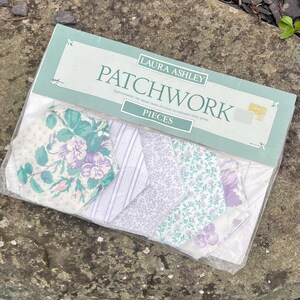 Pode incluir: Um pacote de pe&ccedil;as de patchwork Laura Ashley. As pe&ccedil;as de tecido apresentam desenhos florais e estampados em tons de roxo, verde e branco. A embalagem est&aacute; rotulada como "PATCHWORK" e "PIECES".