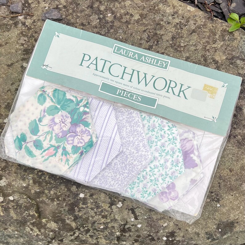 Pode incluir: Um pacote de pe&ccedil;as de patchwork Laura Ashley. As pe&ccedil;as de tecido apresentam desenhos florais e estampados em tons de roxo, verde e branco. A embalagem est&aacute; rotulada como "PATCHWORK" e "PIECES".