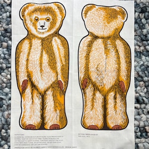 May include: A fabric panel featuring a front and back view of a teddy bear design in shades of brown and tan. The bear has brown paws and a detailed fur pattern. Text at the bottom includes instructions and museum information.