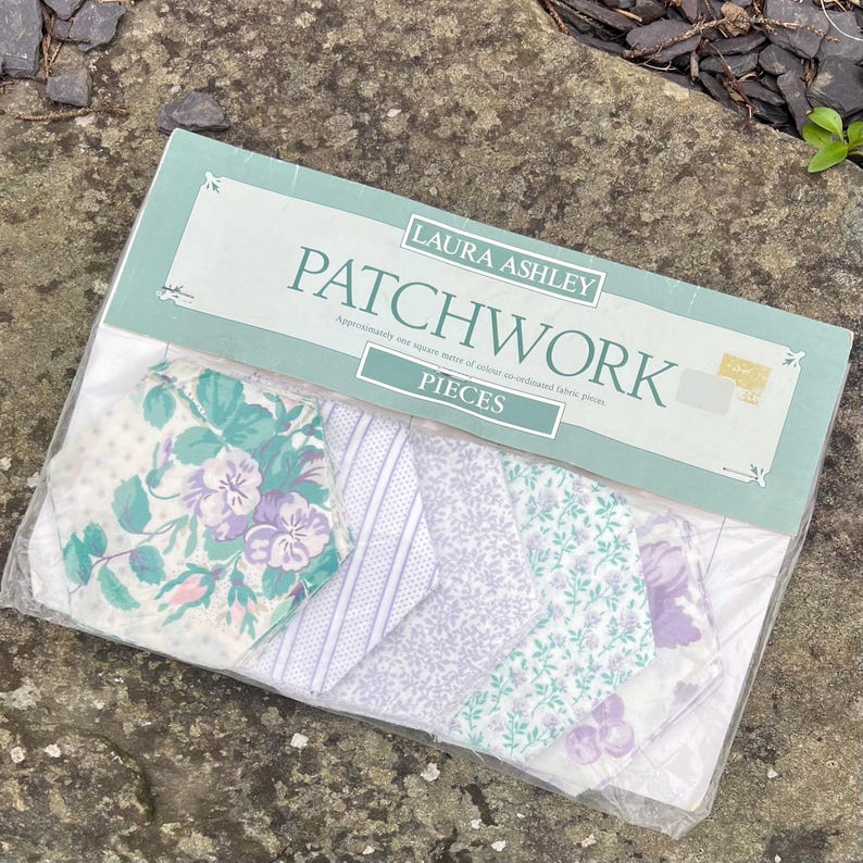 Pode incluir: Um pacote de pe&ccedil;as de tecido patchwork Laura Ashley. As pe&ccedil;as de tecido apresentam v&aacute;rios desenhos florais e estampados, incluindo branco, roxo e verde-azulado. A embalagem est&aacute; rotulada como "PATCHWORK" e "PIECES".