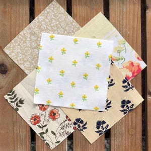 May include: Five fabric squares with different floral patterns. The squares are beige, white, and cream with yellow, red, and blue floral designs.