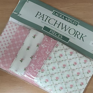 May include: A pack of Laura Ashley patchwork fabric pieces. The fabric displays a variety of pink and white patterns, including floral and geometric designs. The packaging reads "PATCHWORK" and "PIECES".