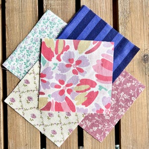 May include: Four fabric squares with different patterns. One square is blue with white stripes, one is pink and white with floral designs, one is beige with a floral pattern, and one is pink with a floral pattern.