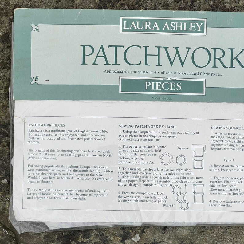 Pode incluir: Um pacote de pe&ccedil;as de tecido patchwork Laura Ashley. O texto diz: "Aproximadamente um metro quadrado de pe&ccedil;as de tecido coordenadas por cores". Inclui instru&ccedil;&otilde;es para costurar patchwork &agrave; m&atilde;o e pe&ccedil;as quadradas.