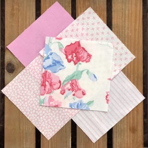 May include: Four pink and white fabric squares with different patterns. The squares are arranged in a diamond shape. The patterns include a floral design, a small pink dot pattern, a larger pink dot pattern, and a pink and white stripe pattern.