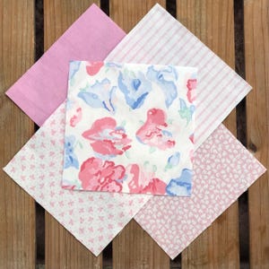 May include: Five fabric squares in various pink and white patterns. The squares are arranged in a star shape. The patterns include a floral print, a striped print, a small floral print, and two solid pink prints.