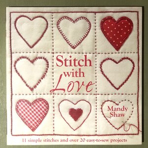 Peut inclure: Couverture de livre avec le titre "Stitch with Love" en lettres rouges et blanches. La couverture présente une grille de neuf cœurs, chacun avec un motif de point différent. Les cœurs sont rouges, blancs et en vichy rouge et blanc. Le nom de l'auteur, "Mandy Shaw", est imprimé dans le coin inférieur droit.