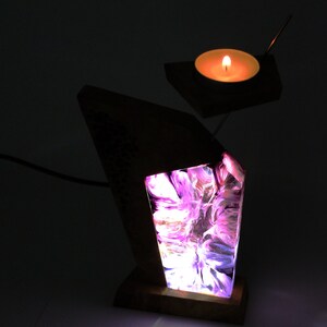 Peut inclure: Une lampe en bois unique avec un design abstrait lumineux dans les tons de violet, rose et blanc. Un petit bougeoir avec une bougie allum&eacute;e est suspendu au-dessus de la lampe. La lampe est aliment&eacute;e par un cordon.
