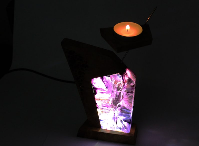 Peut inclure: Une lampe en bois unique avec un design abstrait lumineux dans les tons de violet, rose et blanc. Un petit bougeoir avec une bougie allum&eacute;e est suspendu au-dessus de la lampe. La lampe est aliment&eacute;e par un cordon.