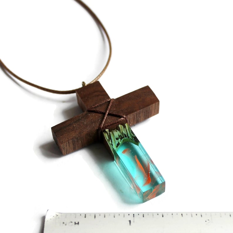 May include: A wooden cross necklace with a blue and orange resin inlay. The cross is tied with brown string and hangs from a brown leather cord.